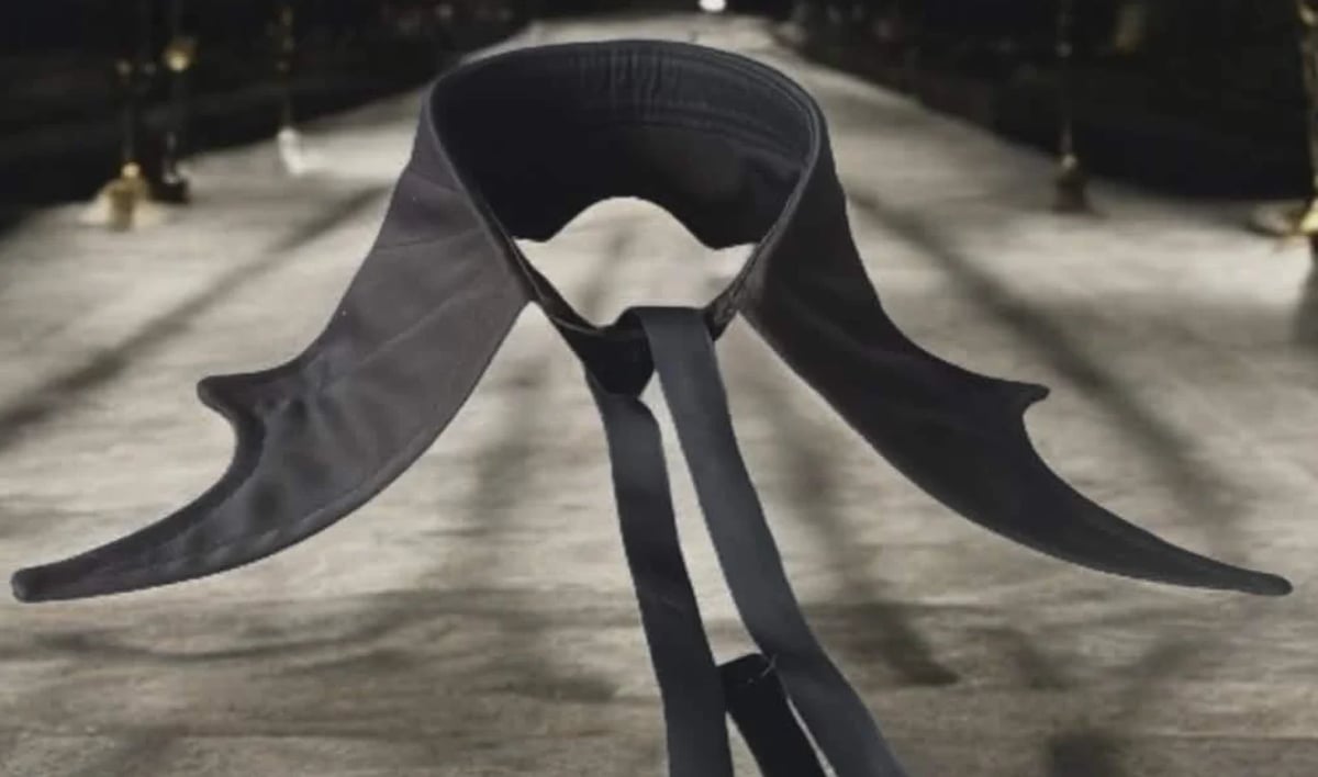 Black fabric with large wing-like shapes and trailing ribbon strands laid out on pavement in sunlight