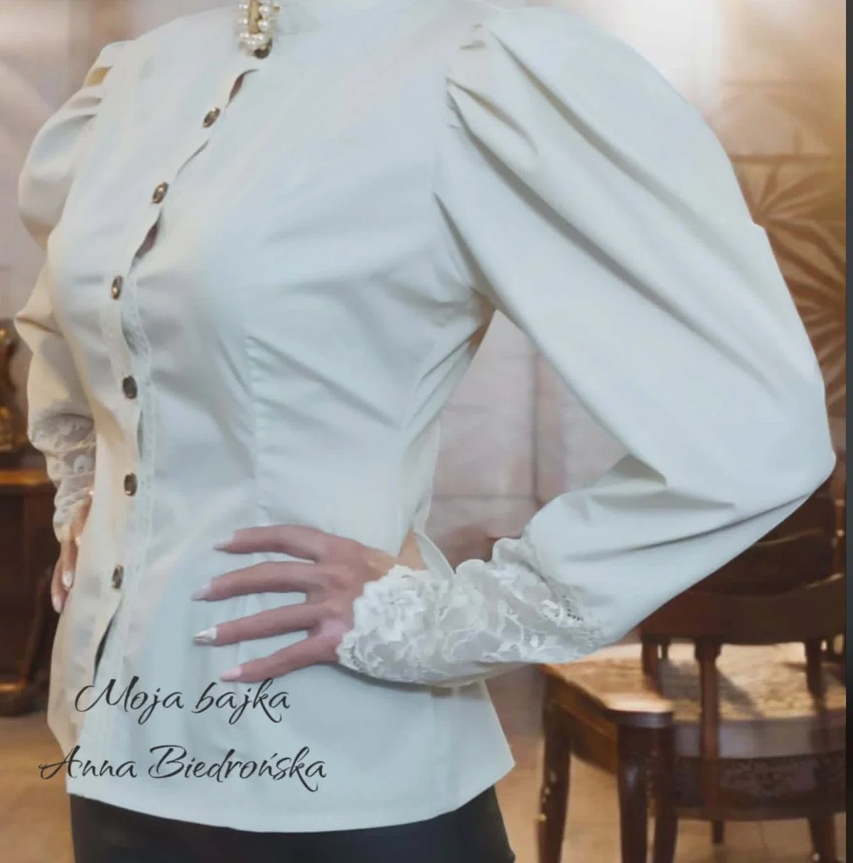 Woman wearing a white button-up blouse with lace cuff details and pearl accents on the sleeve