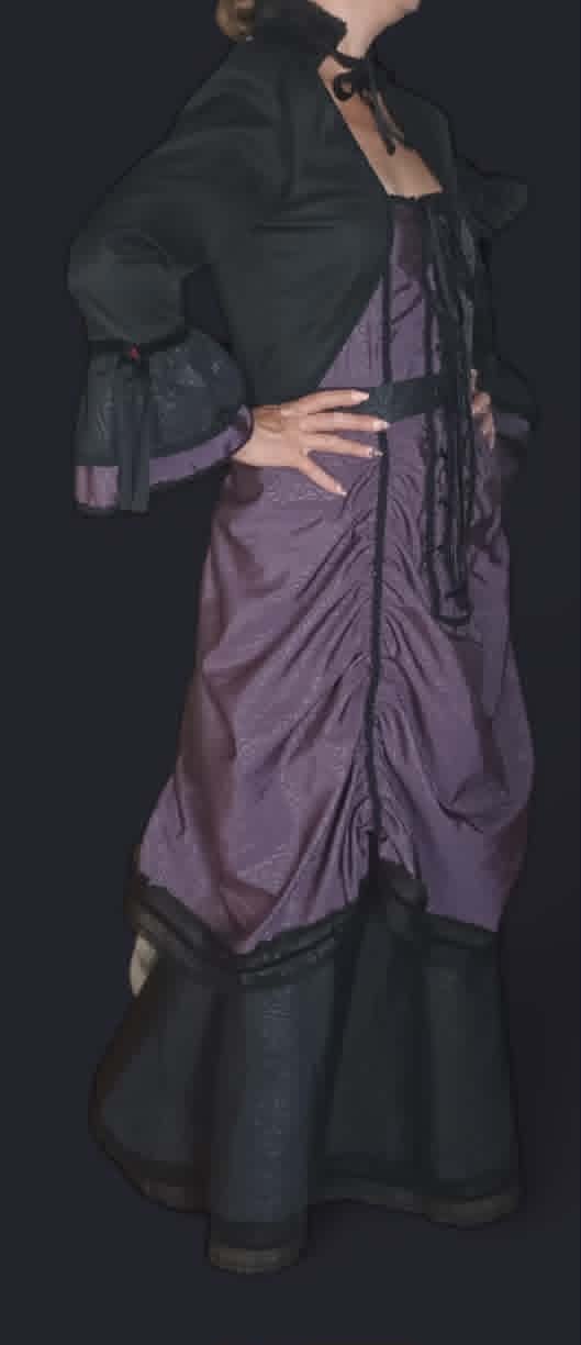 Woman wearing a dark green blazer over a purple wrap dress with black boots, posed against a dark background