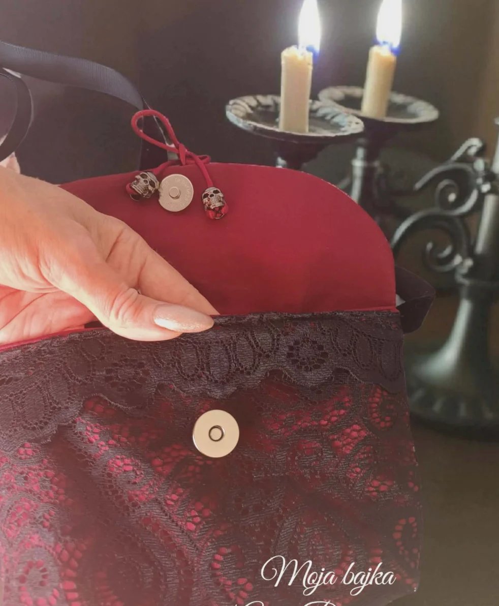 Hand holding red decorative pouches with beaded ornaments, lit candles in background