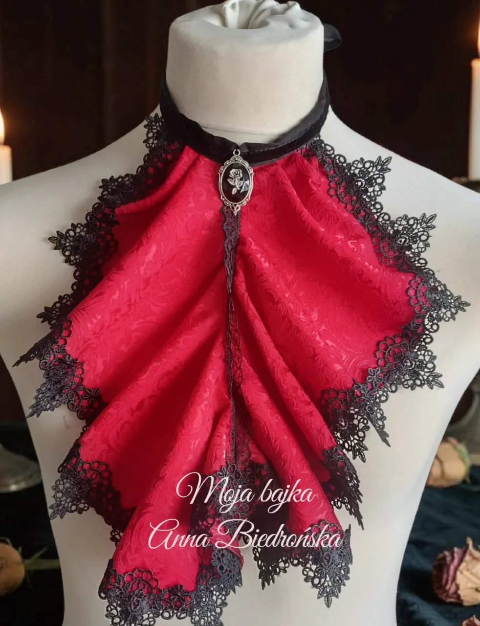 Red velvet bow tie with black lace trim and silver pendant charm displayed on a mannequin