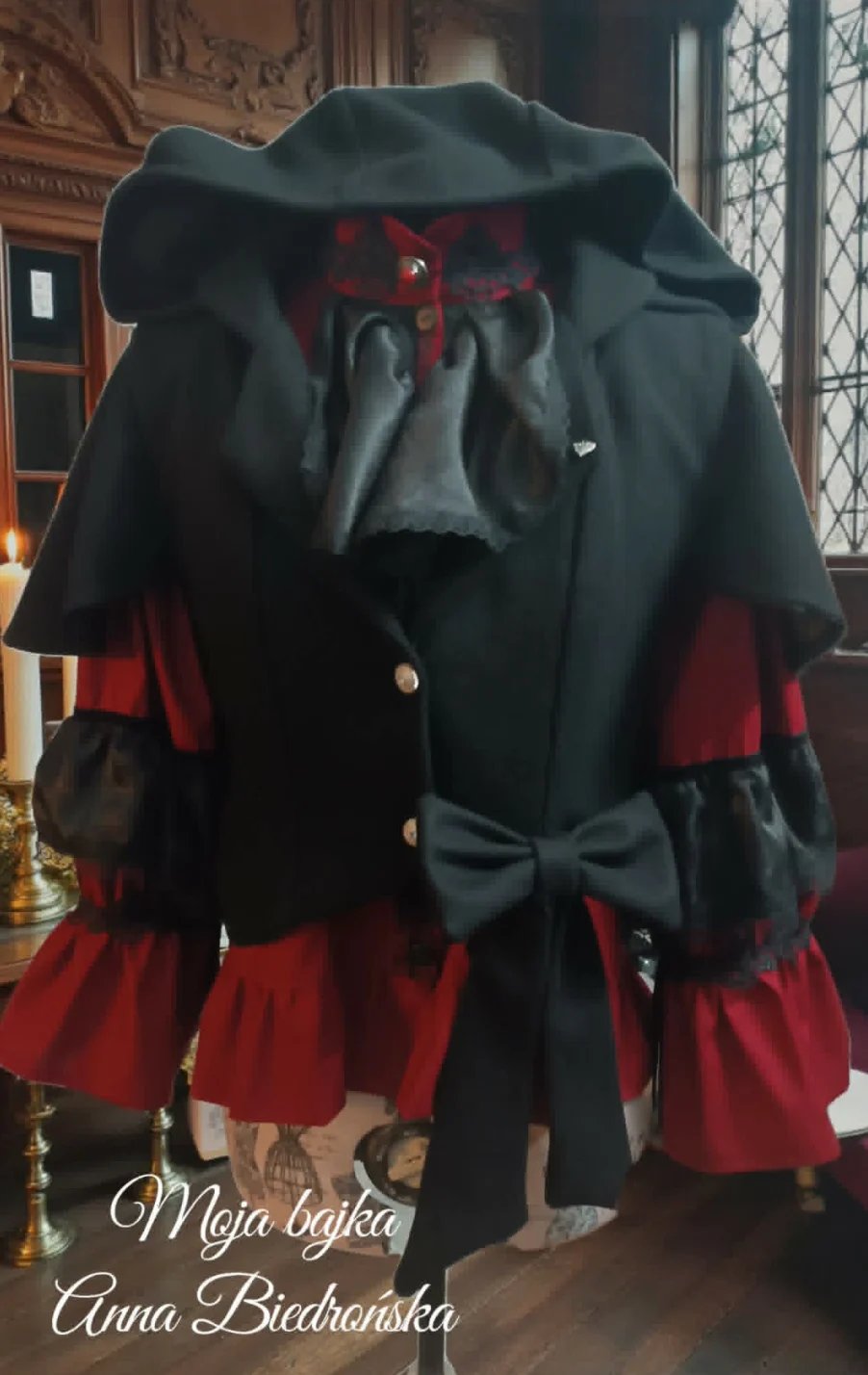 Elegant dress form displaying a black and red gown with wide-brimmed black hat and black bow detail in a formal interior