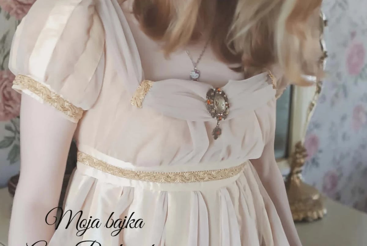 Close-up of a person wearing a white chiffon dress with gold beaded waistband and off-shoulder sleeves, featuring ornate jewelry
