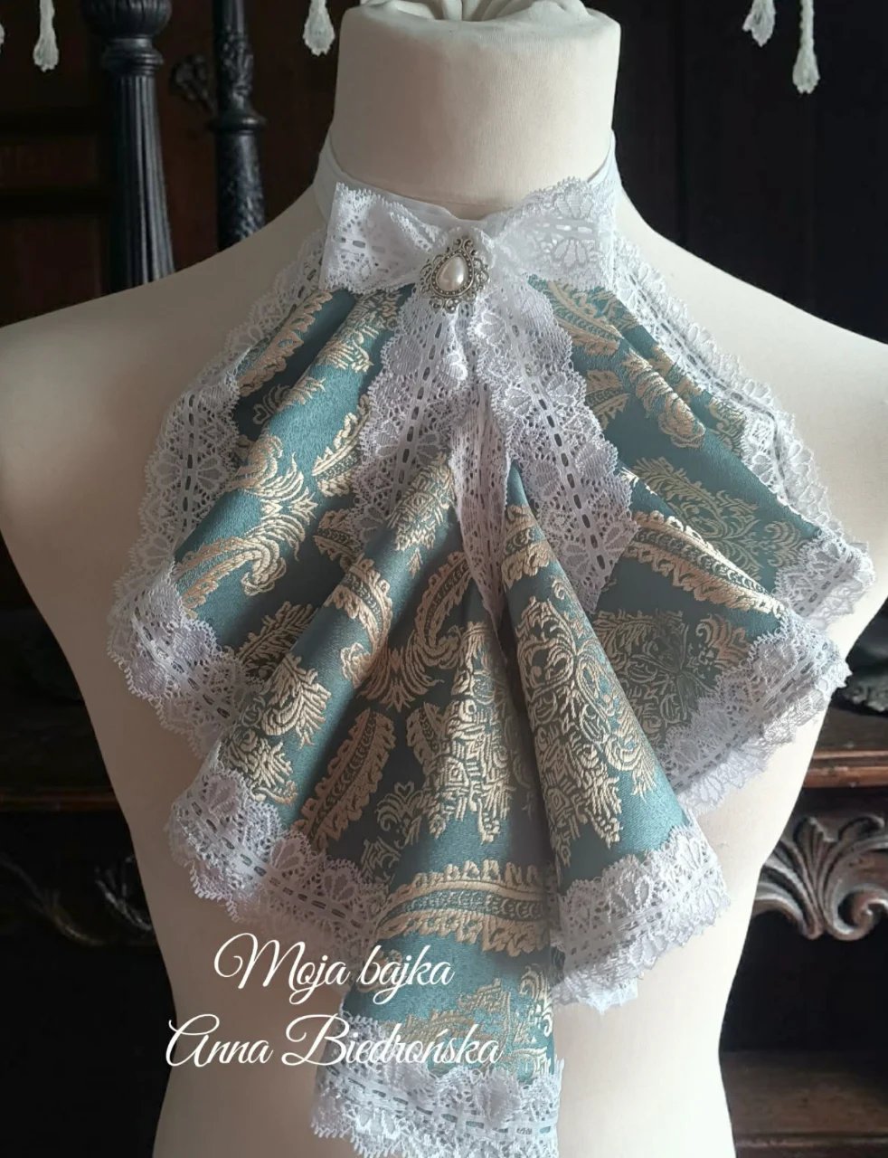 Ornate lace bow with teal and gold patterned fabric center on ivory dress form