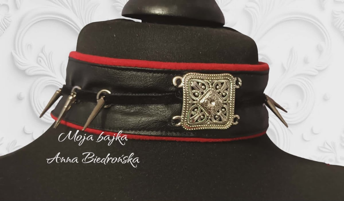 Black wide collar necklace with red trim, ornate square buckle, and charms on mannequin bust