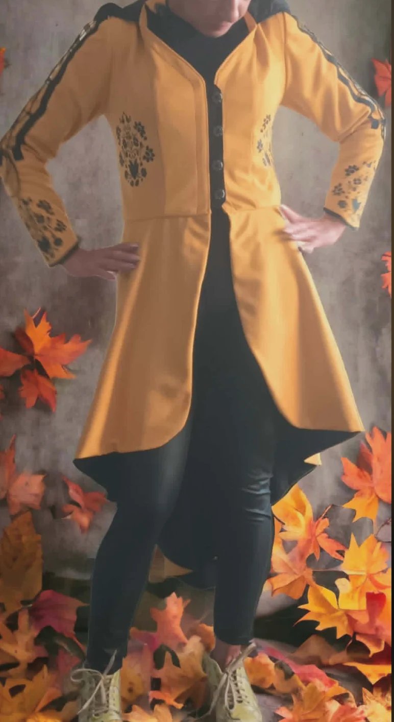 Person wearing a gold embroidered duster cardigan over black clothing, posed against a gray background with autumn leaves