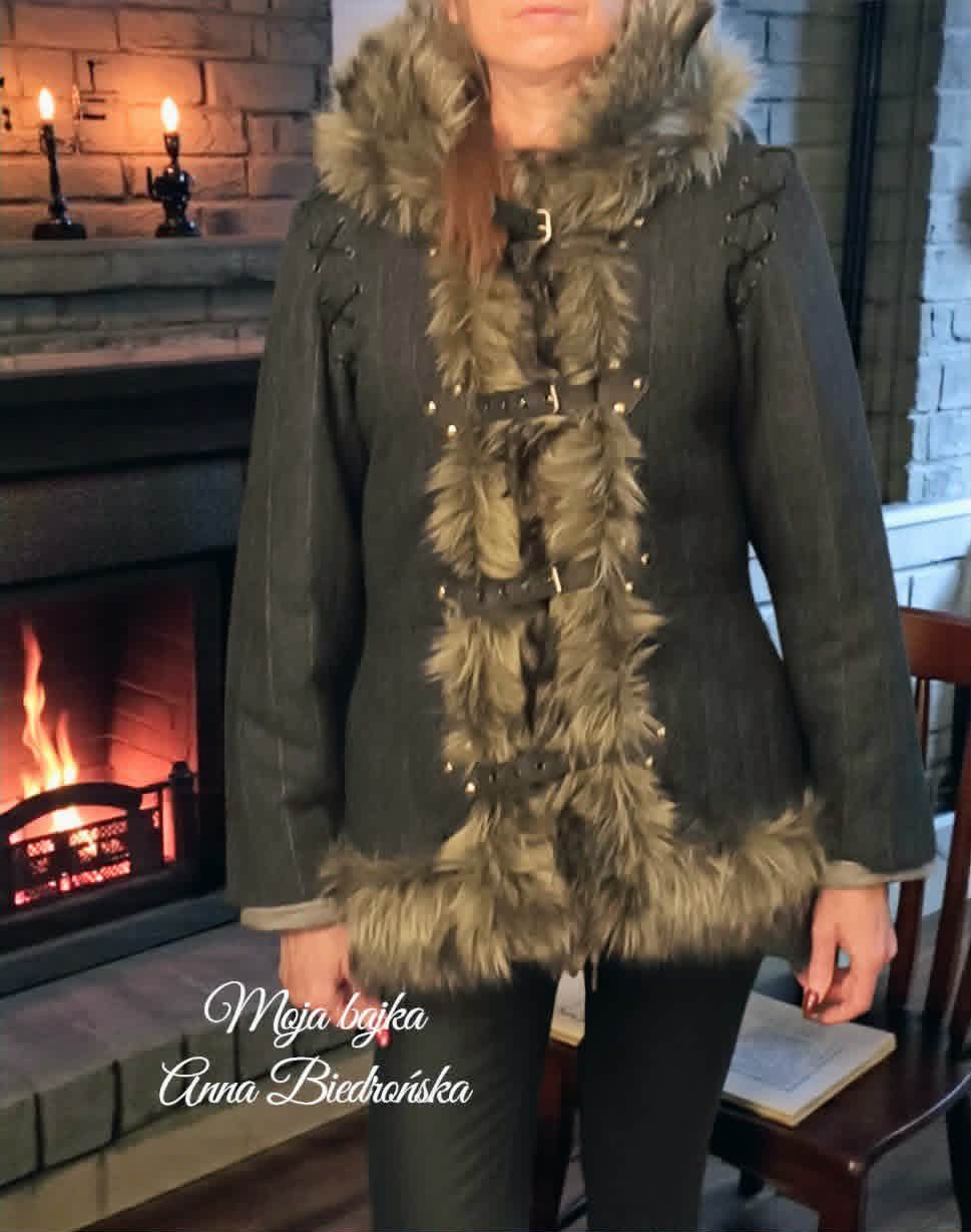 Woman wearing olive green jacket with fur trim standing by fireplace in elegant interior setting