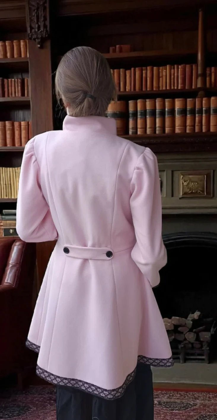 Woman in pink blazer viewed from behind standing in front of wooden bookshelves in a library