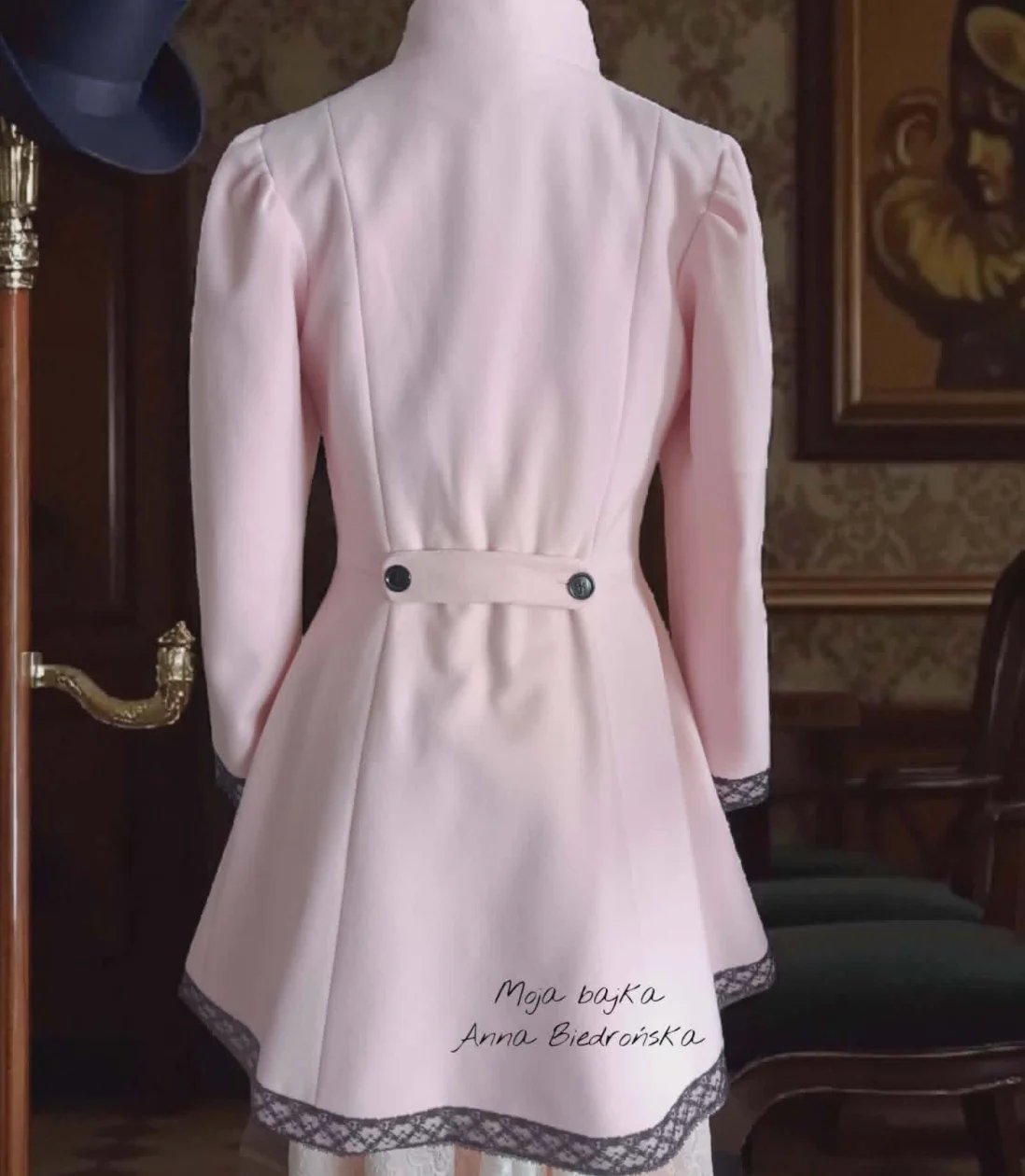 Back view of a light pink blazer dress with long sleeves, cinched waist with dark buttons, and lace trim hem