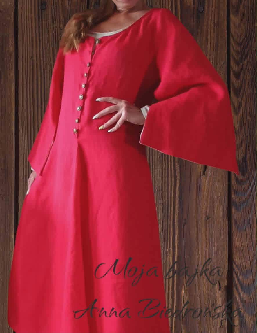 Woman wearing a red medieval-style tunic with wide sleeves and decorative buttons, standing against a dark wooden background