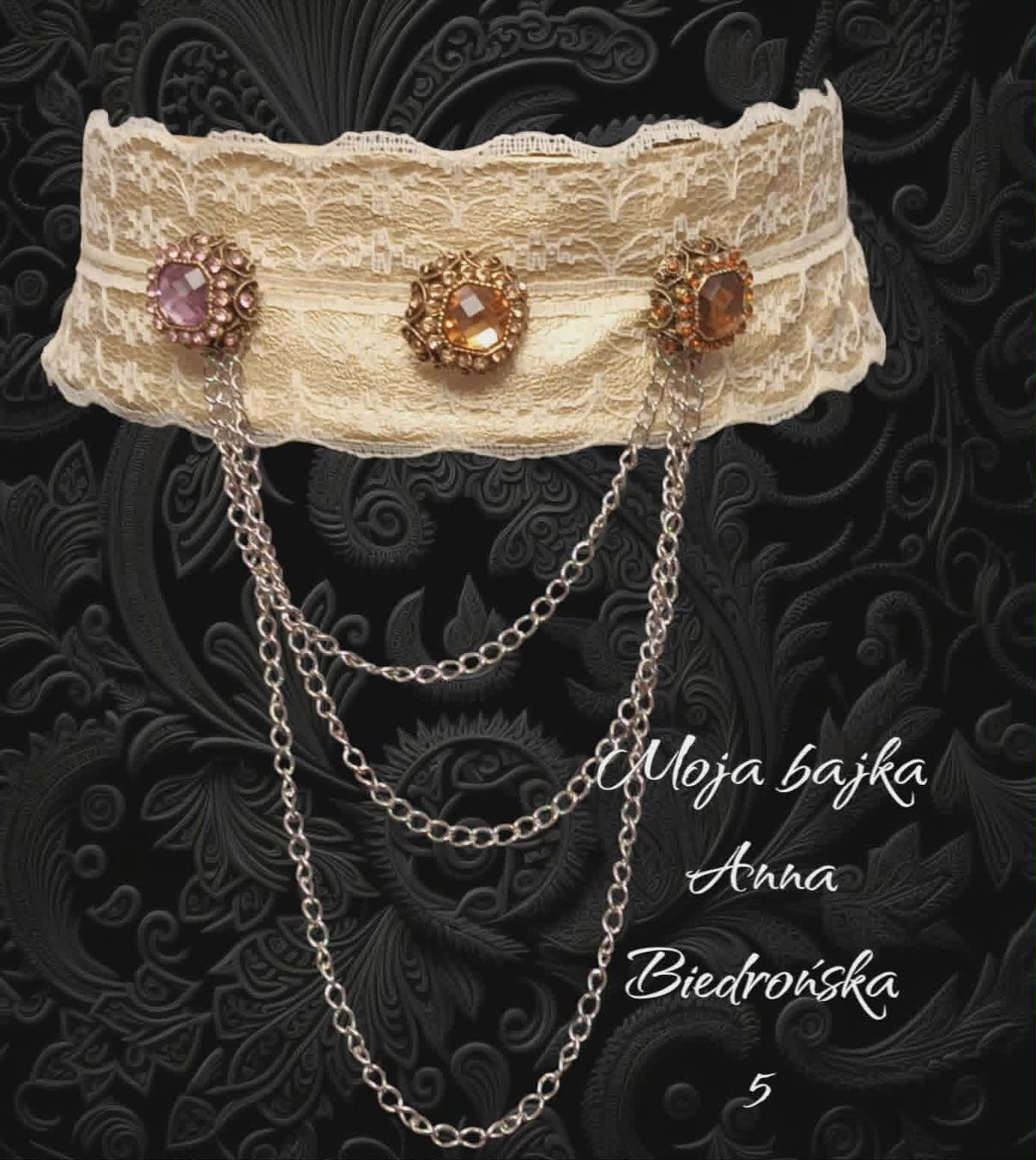 Cream lace choker with three ornate gemstone pendants and draping silver chains on black damask background
