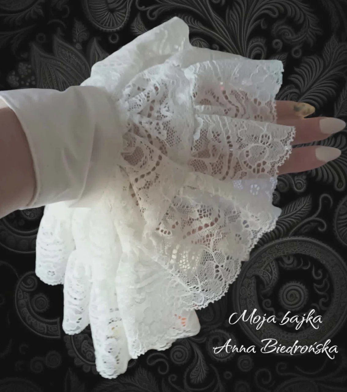 Hand wearing delicate white lace fingerless gloves on dark ornate fabric background