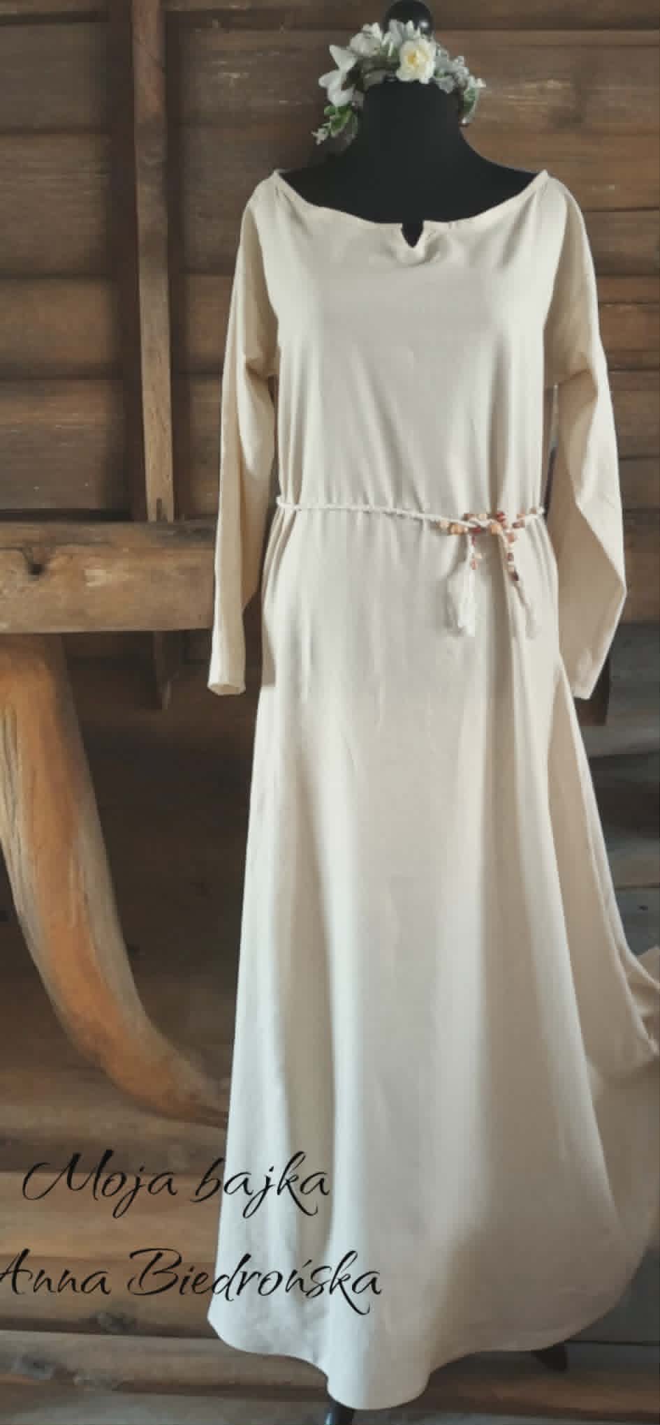 Mannequin wearing cream-colored long dress with belt and floral crown in wooden interior setting