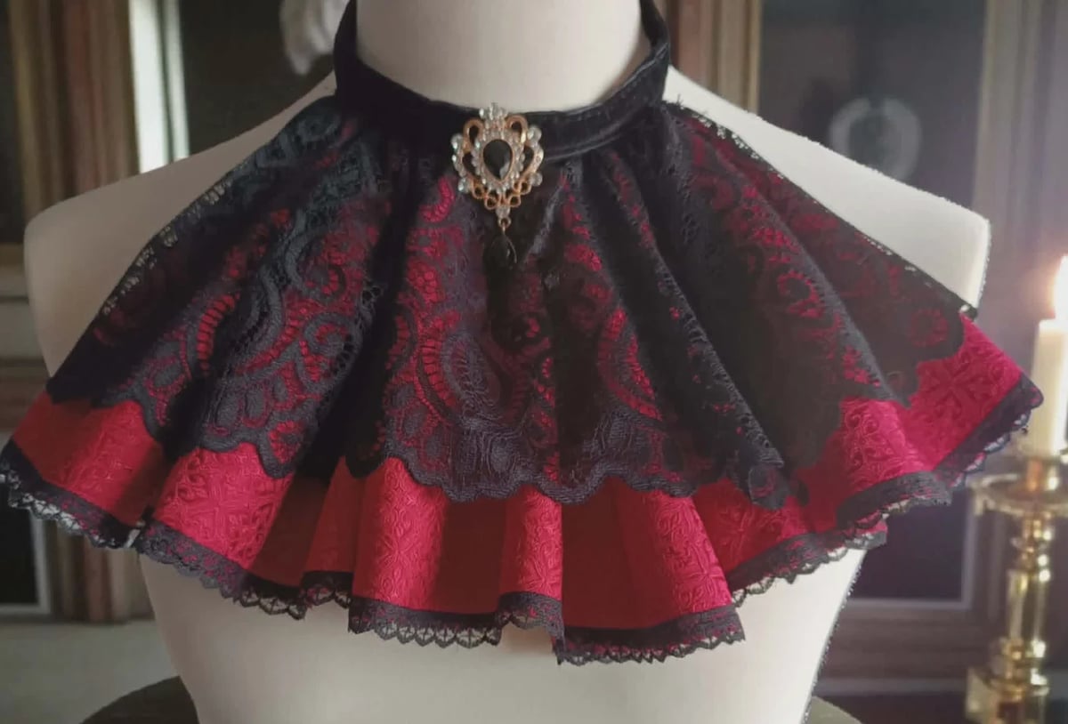 Red and black ornate cape with lace trim displayed on a mannequin torso