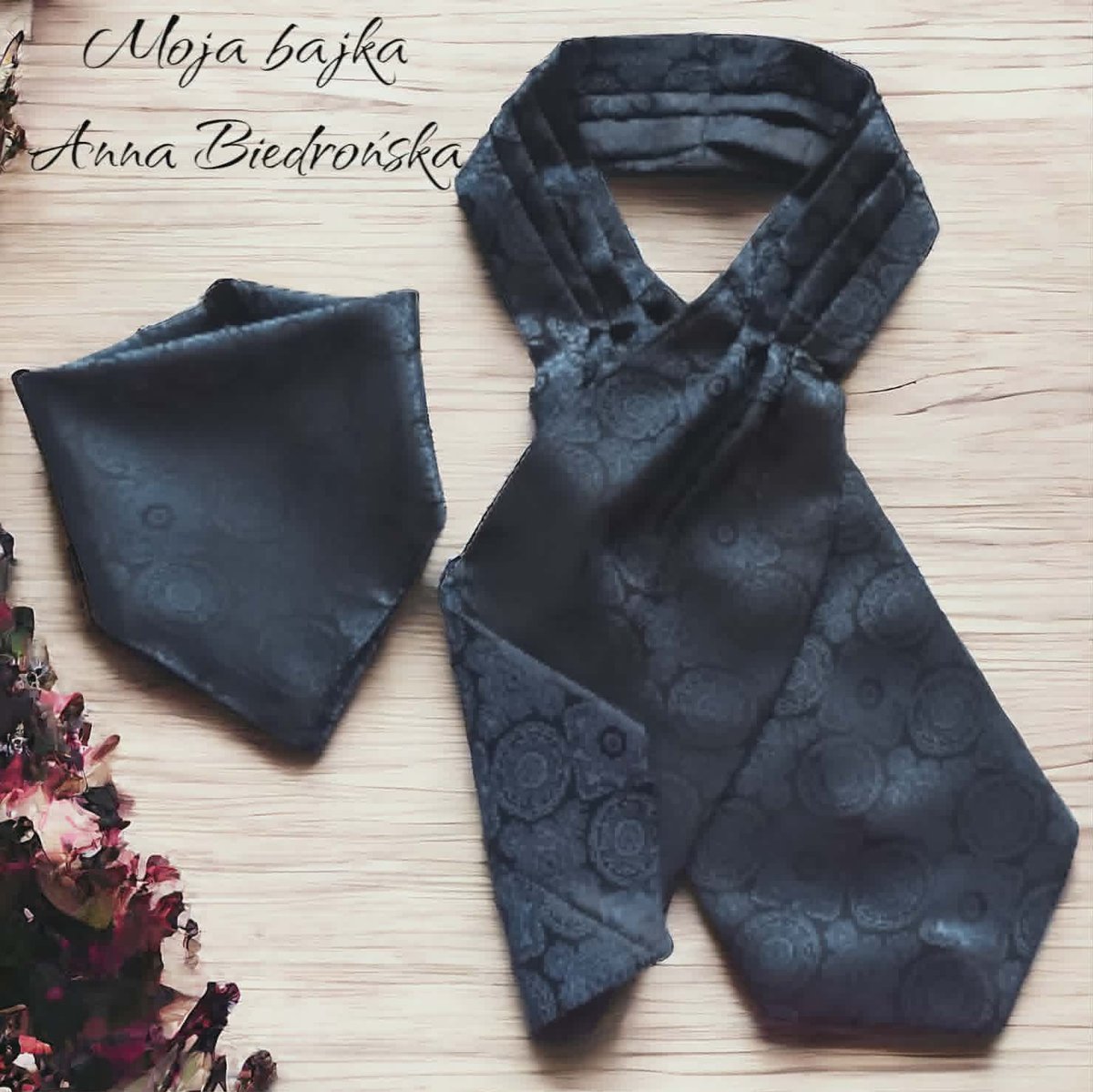 Flat lay of dark blue jacquard cravat and pocket square set with rose pattern on wooden surface with dried flowers