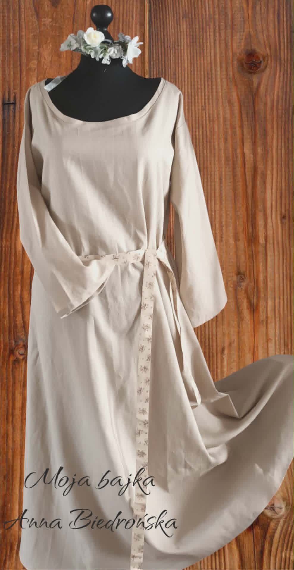 Cream-colored wrap dress on mannequin with white flowers, wooden background, designer text overlay