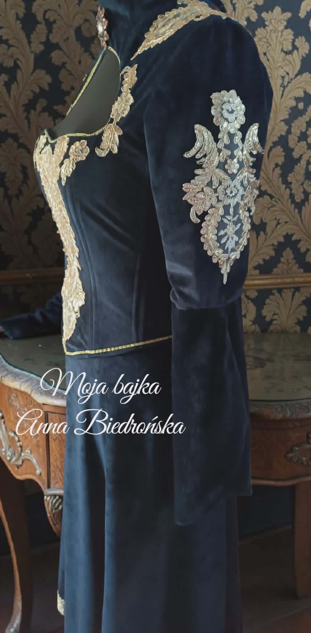 Navy blue velvet dress with ornate gold lace embroidery and decorative trim displayed on a mannequin against damask wallpaper