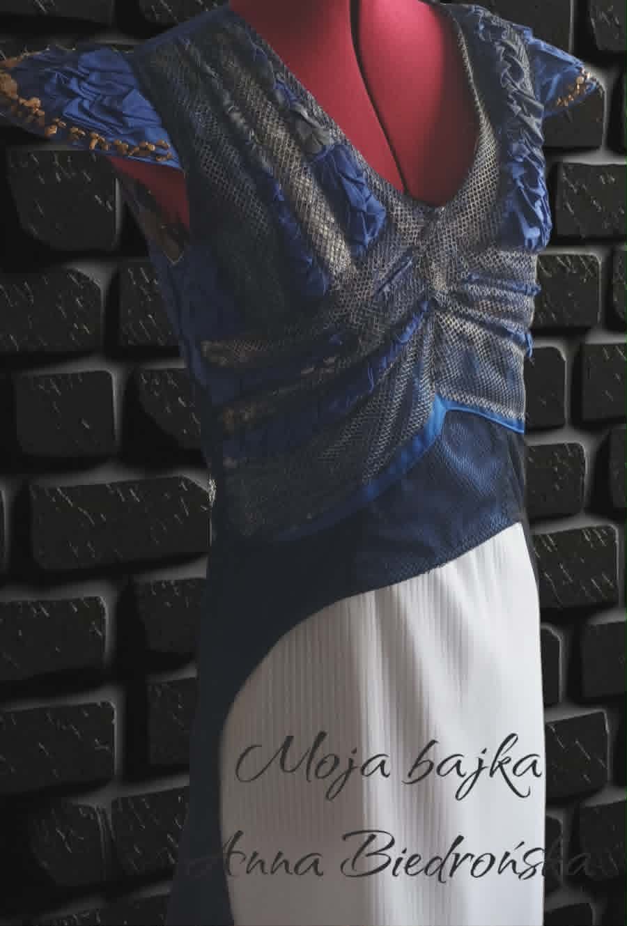 Model wearing blue and white dress with script text, posing against dark brick wall background
