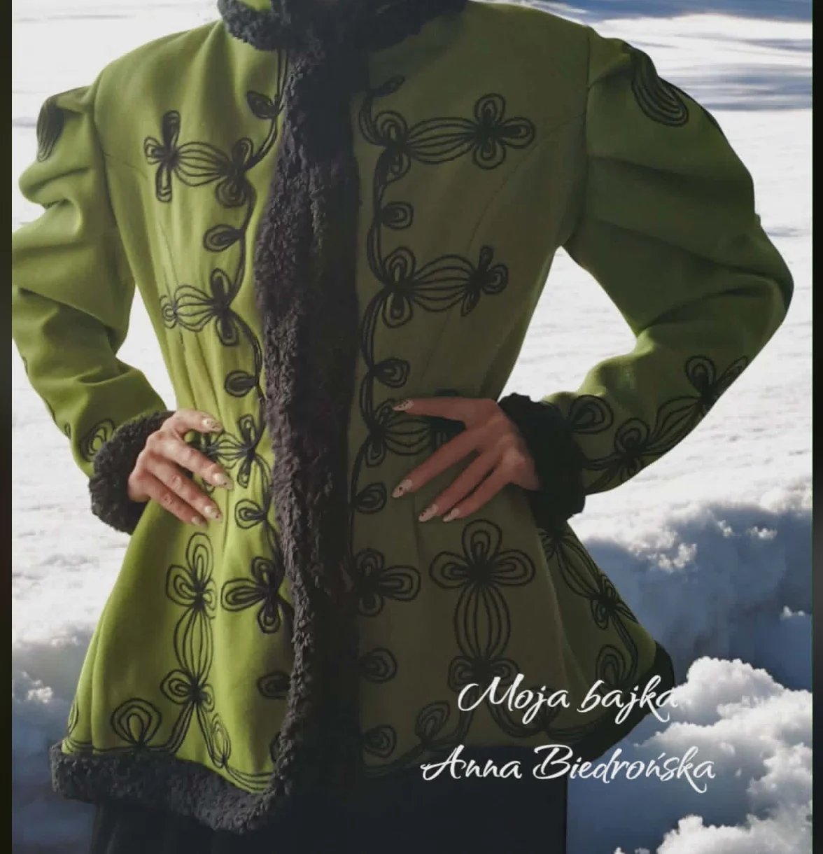 Person wearing lime green embroidered coat with black ornamental patterns and dark lace trim, standing against cloudy sky background