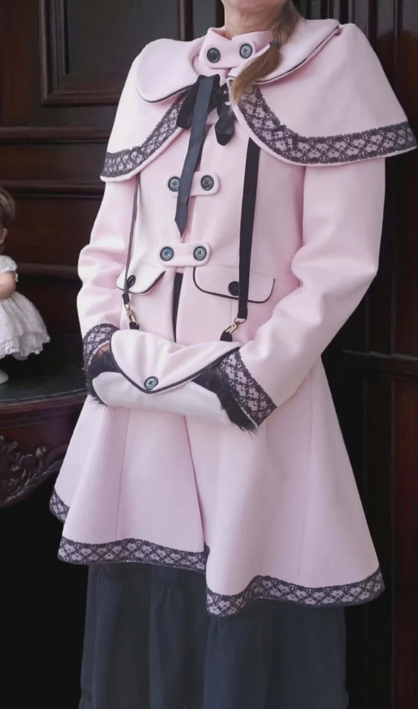 Woman wearing a pink vintage-style coat with lace trim, matching capelet, and black ribbon bow detail