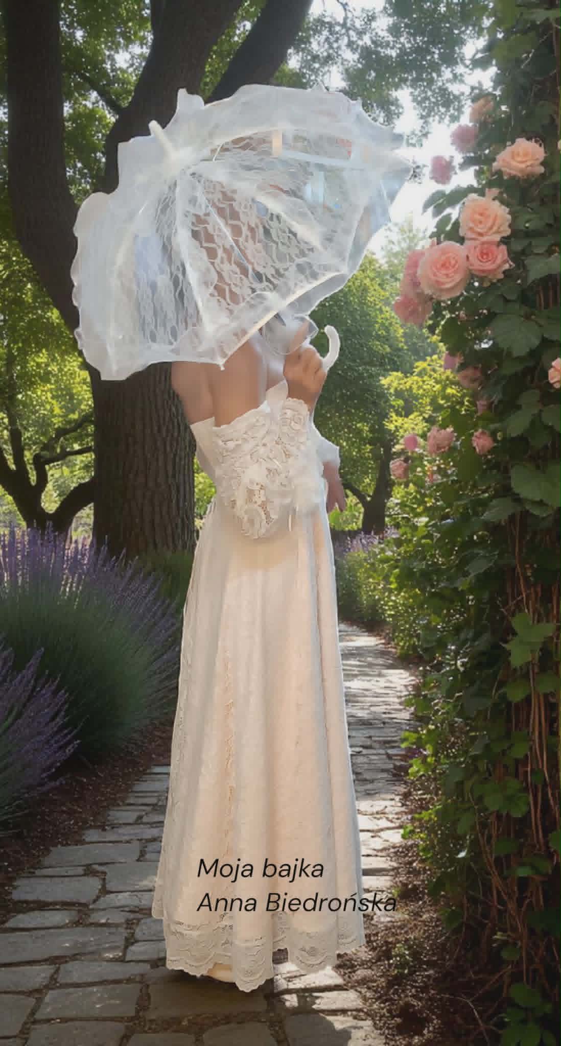 Woman in white lace wedding dress holding decorative parasol in garden with pink roses and flowering plants