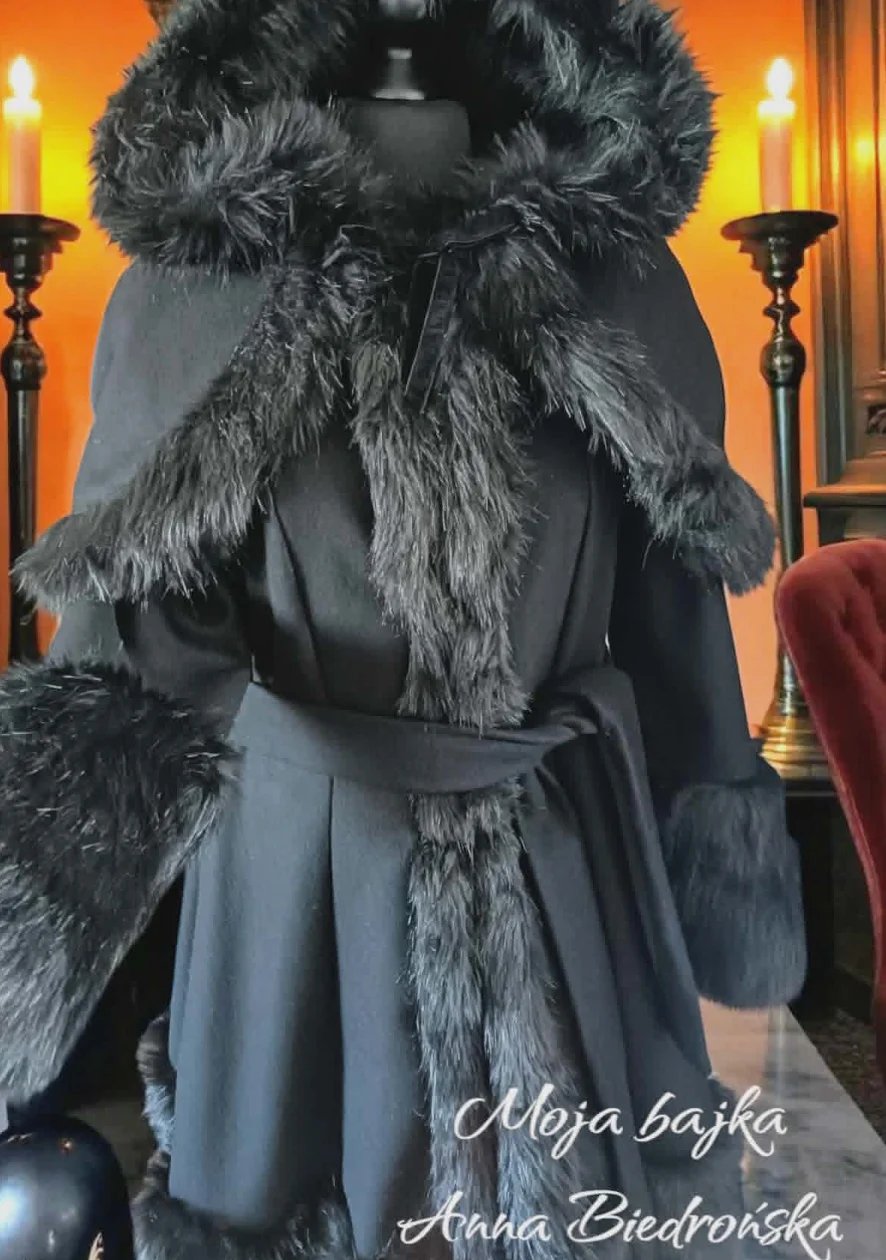 Elegant black coat with fur collar and cuffs on dress form in warm-toned elegant interior setting