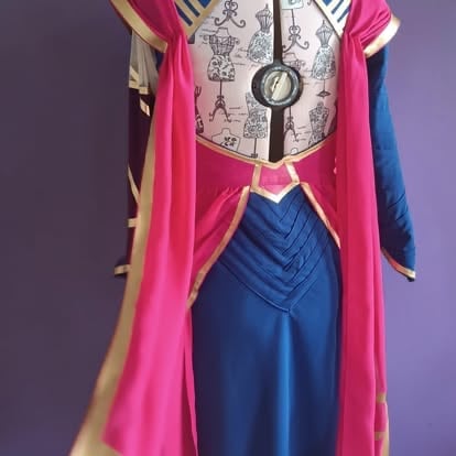 Cosplay costume display featuring a pink cape, blue dress, and white graphic top with a pendant necklace