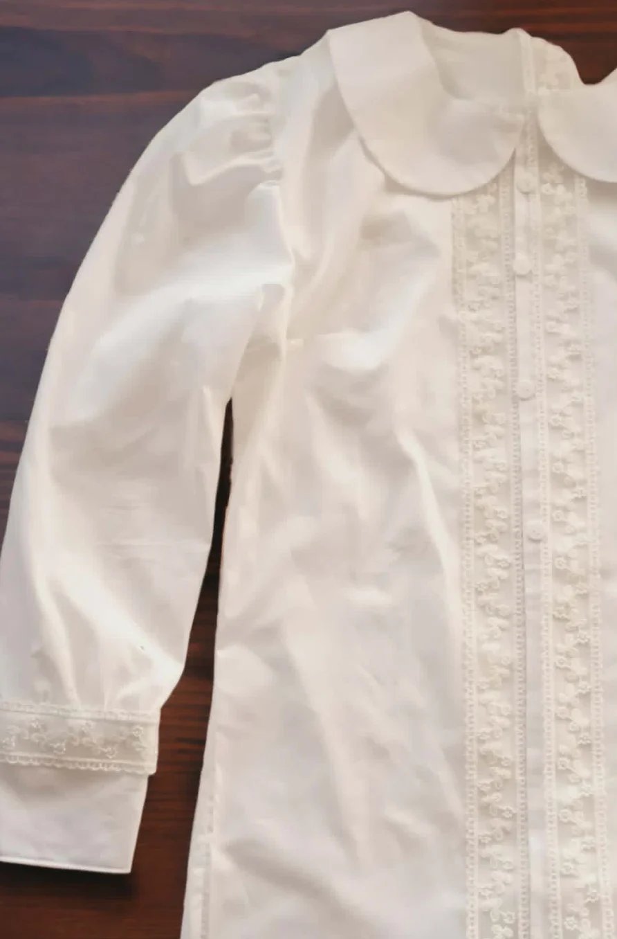 White vintage blouse with puffed sleeves, peter pan collar, and delicate lace front detailing draped on wooden surface
