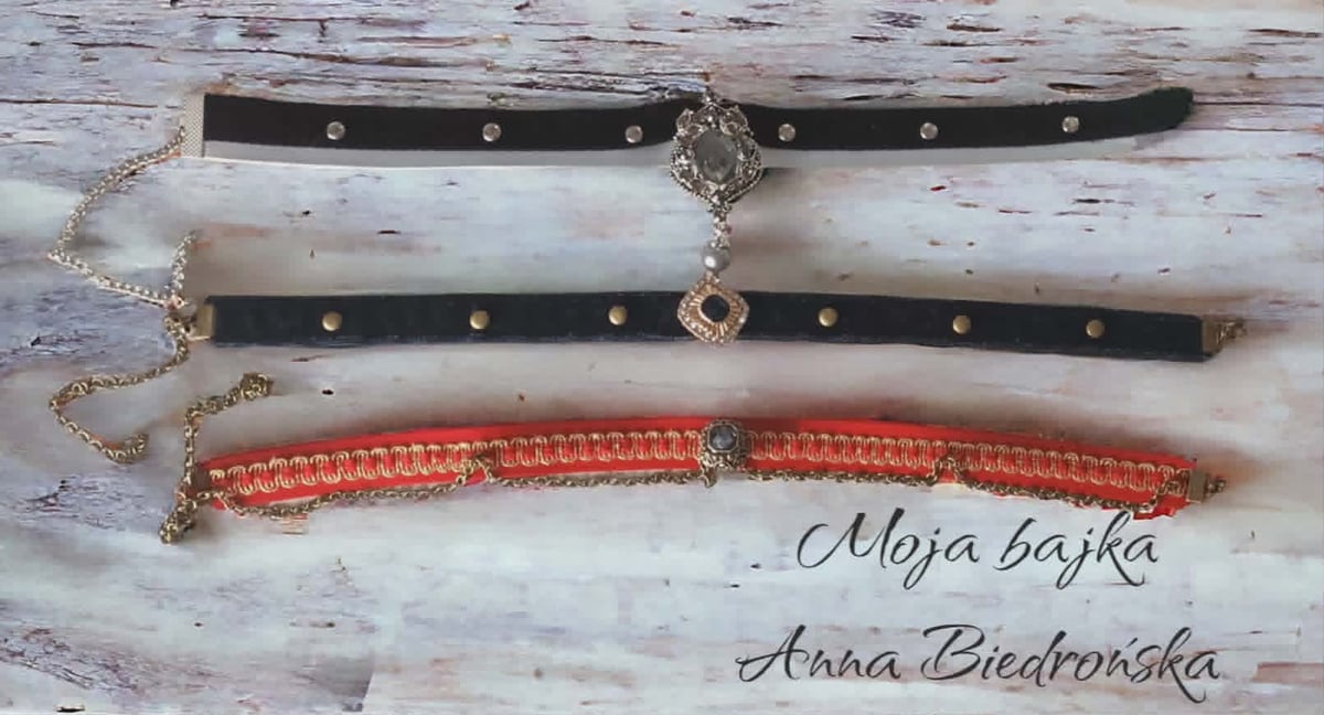 Three studded choker necklaces in black, white, and orange laid on a white wooden surface with artist names