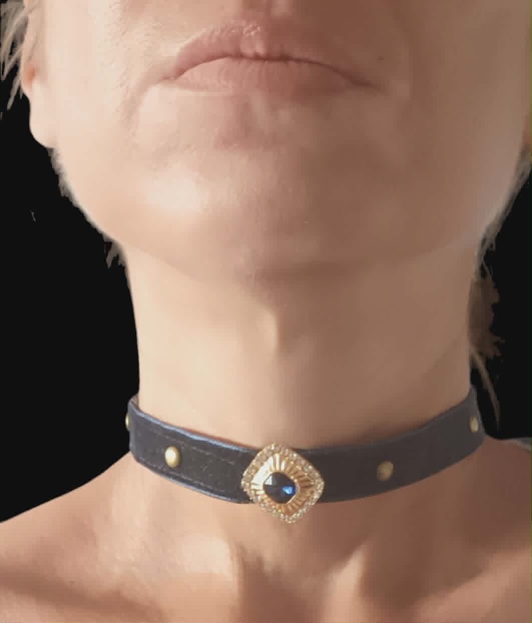 Close-up of a person wearing a black leather choker with a decorative gold and gemstone pendant