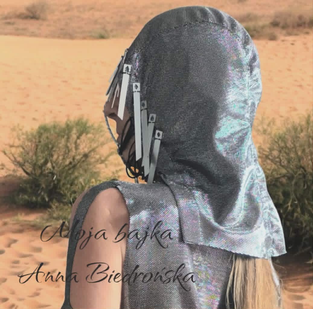 Person wearing headphones with fabric draped over their head in a desert landscape with sparse vegetation