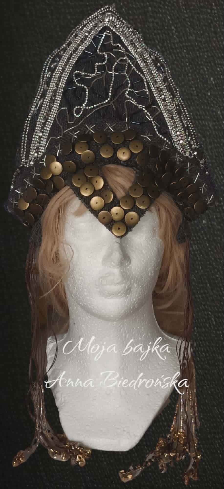 Marble bust sculpture wearing ornate beaded headdress with filigree crown and wooden beads, against dark background