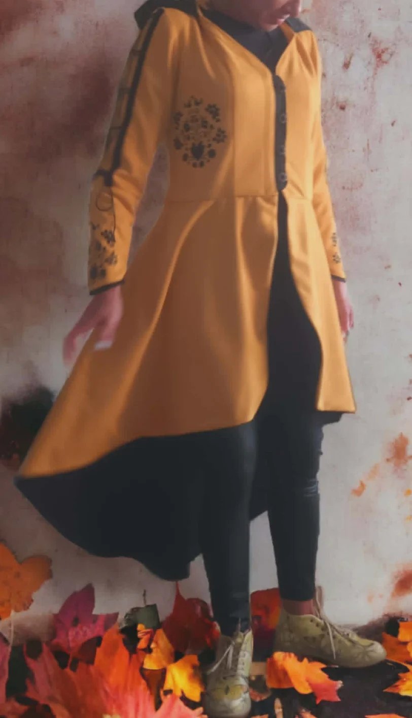 Person wearing a mustard yellow cardigan and black pants surrounded by autumn leaves