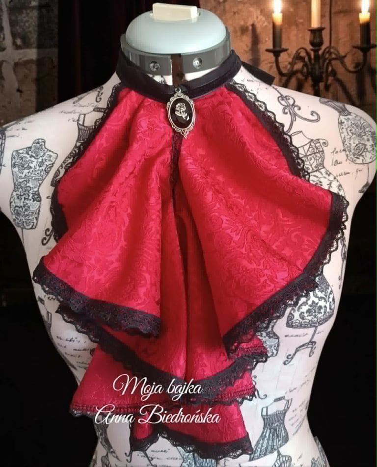 Red velvet bow brooch with black lace trim displayed on dress form mannequin with ornate pattern
