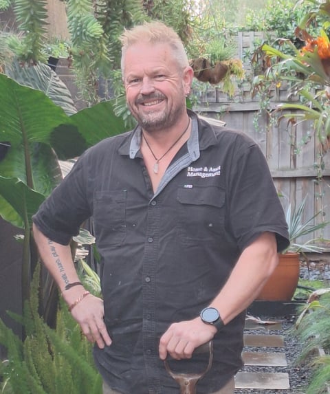 David, Geelong handyman and owner of Home and Asset Management, smiling in a garden with a shovel