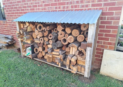 Firewood storage shed - timber log store built against red brick wall by Geelong handyman, filled with cut firewood