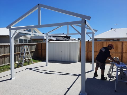 Geelong handyman at work under modern metal pergola structure in backyard with timber fencing and storage shed