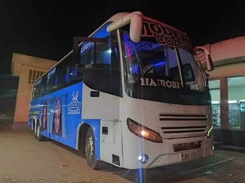 Blue and white intercity bus parked at night with illuminated headlights and signage on its side
