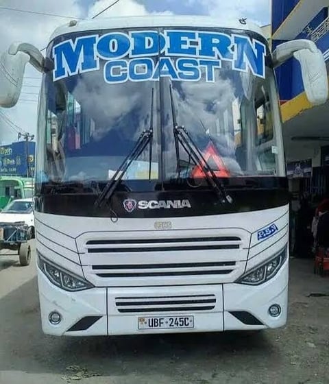 White Scania coach bus with Modern Coast branding on windshield, parked at a depot with license plate visible
