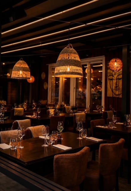 Elegant restaurant dining room with woven pendant lights, dark wood tables, and brown upholstered chairs under warm ambient lighting