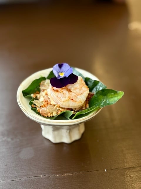 Plated shrimp dish garnished with edible flowers and fresh greens on a small white plate