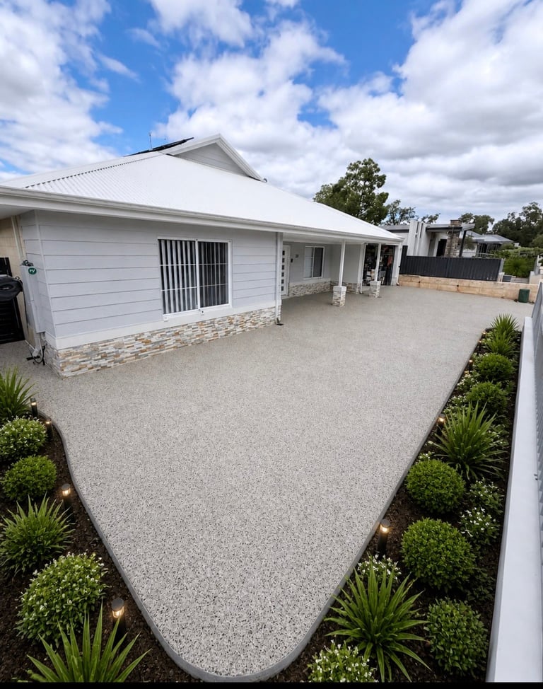 Modern white house with gabled roof, concrete driveway, and landscaped garden under blue sky