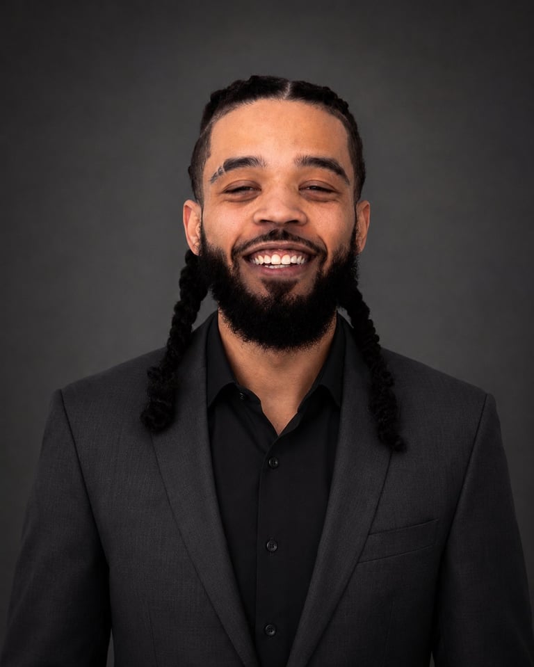 Portrait of a smiling man with a beard wearing a dark blazer and black shirt against a gray background
