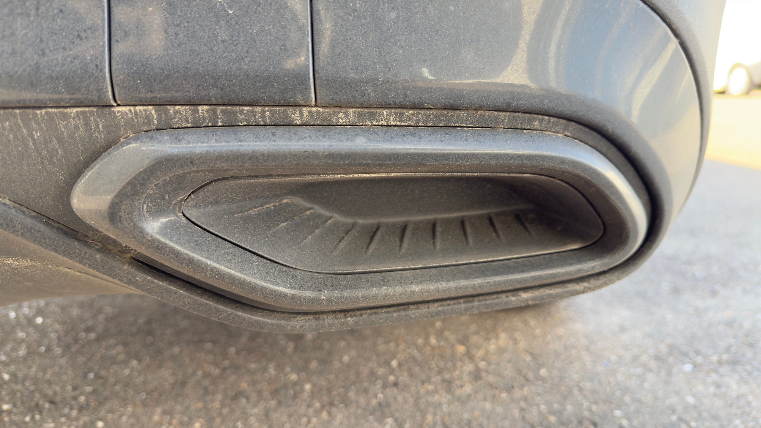 Voor: Close-up of a vehicles exhaust pipe opening showing the oval-shaped muffler outlet with ridged interior detail