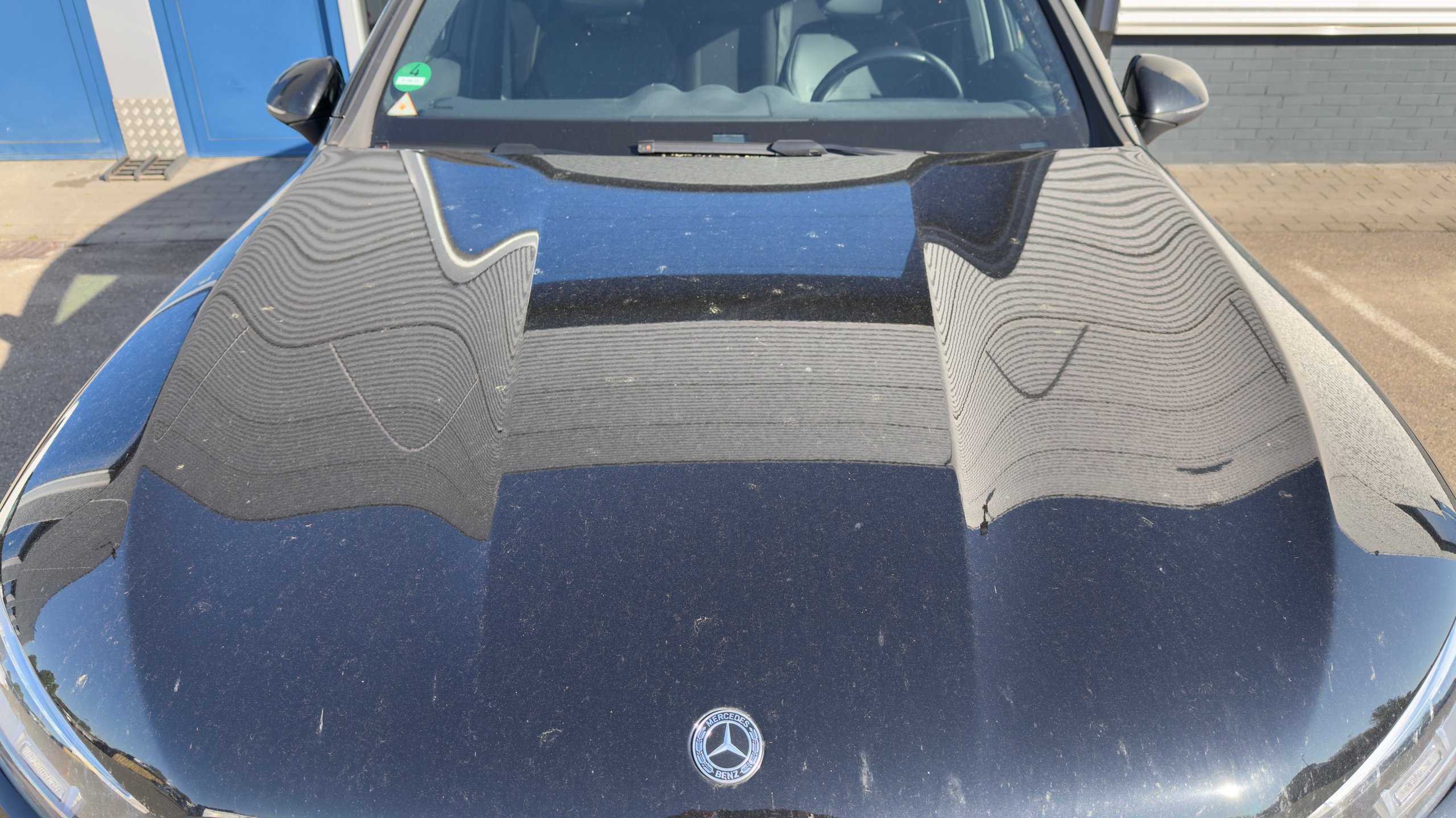 Voor: Hood of blue car showing protective covers and Mercedes-Benz logo on the windshield