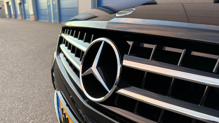 Close-up of a Mercedes-Benz front grille and logo on a black vehicle parked outdoors