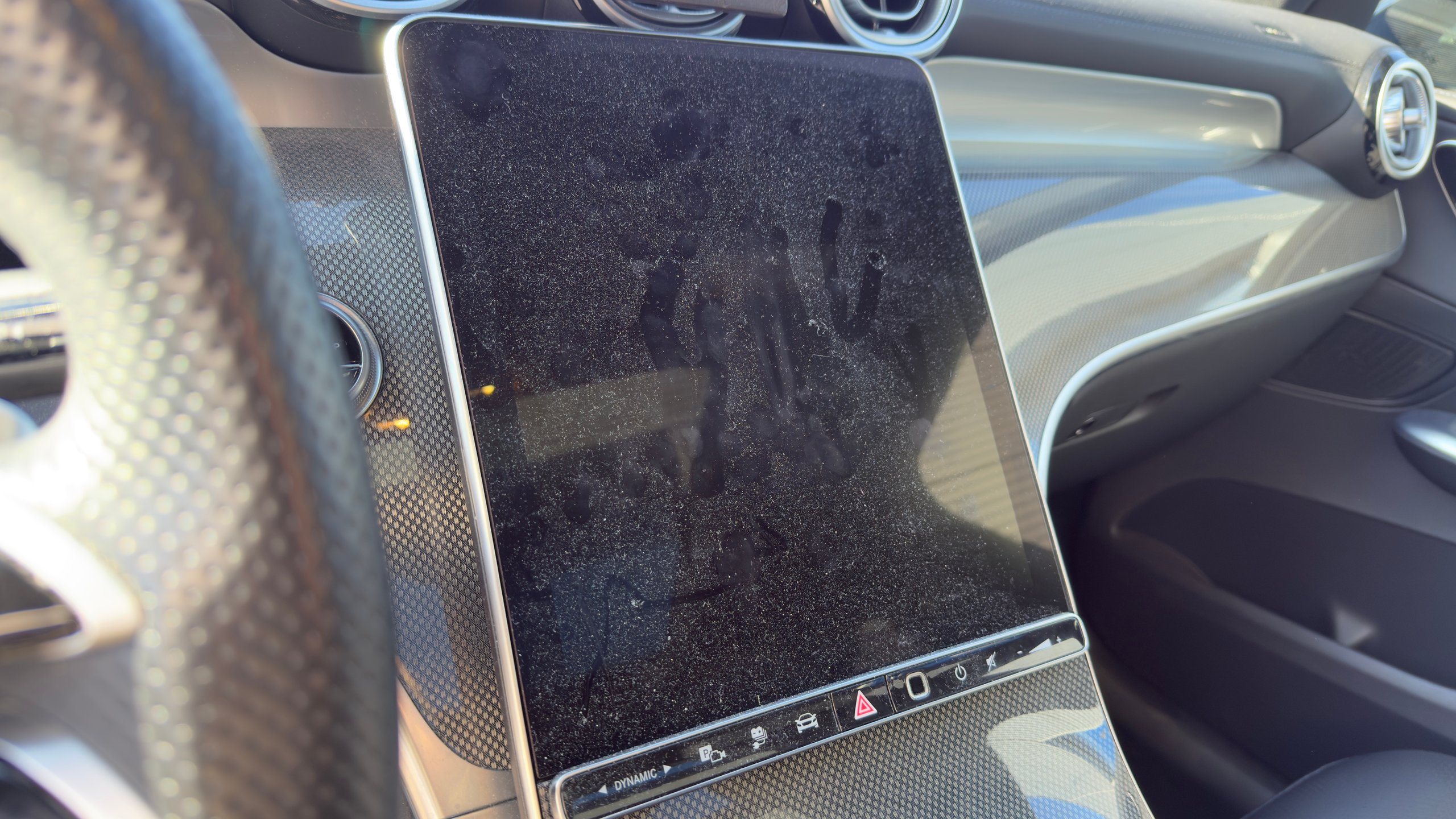 Voor: Car dashboard with dusty touchscreen display and steering wheel visible on left side