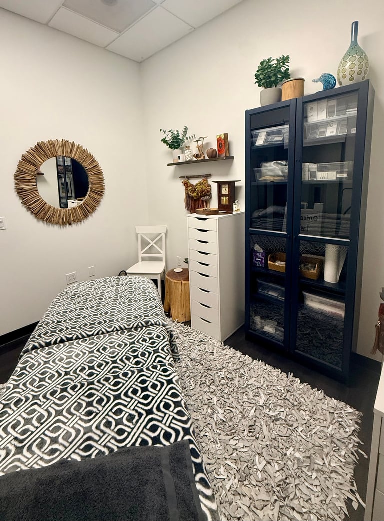 Cozy bedroom with geometric patterned rug, white chair, black glass cabinet, floating shelves with plants, and woven mirror on wall