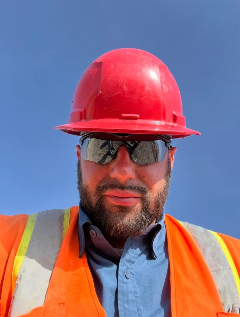Construction worker wearing red hard hat, orange safety vest, and dark sunglasses against clear blue sky