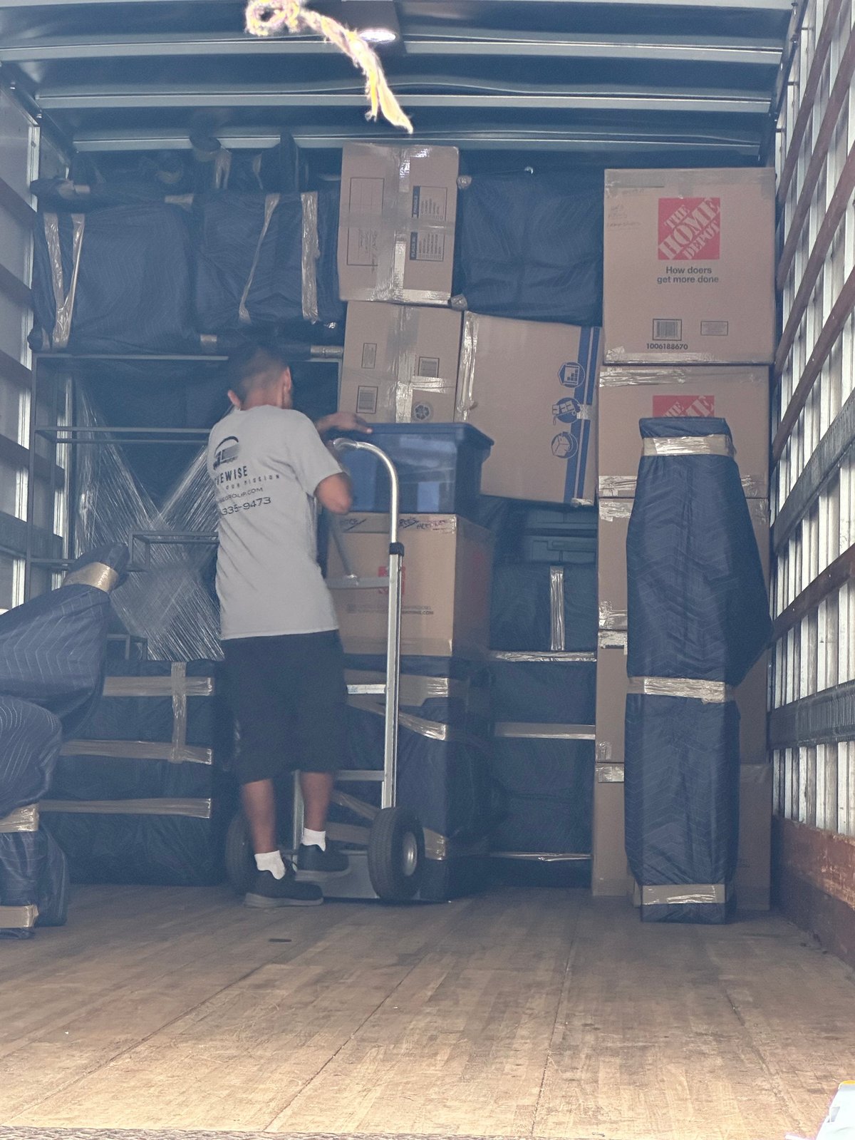 Worker loading cardboard boxes into a moving truck using a hand truck dolly